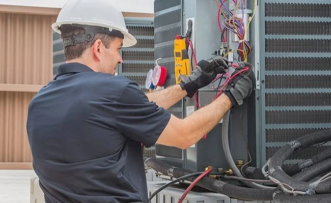 Technician checking the electrical components of an outdoor HVAC unit