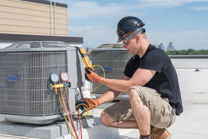 Technician checking rooftop air conditioning equipment with diagnostic gauges